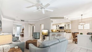 A modern living room with a sofa, TV, and dining area. - Desired Pelican Landing First Floor Coach Home (Bonita Springs)