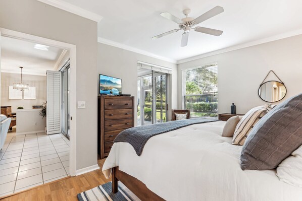A bedroom with a bed, a dresser, a ceiling fan, and a view of the outdoors.