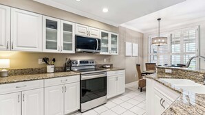A modern kitchen with white cabinets, a stainless steel oven, a microwave, and a granite countertop. - Desired Pelican Landing First Floor Coach Home (Bonita Springs)