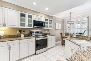 A modern kitchen with white cabinets, a stainless steel oven, a microwave, and a granite countertop.