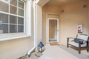 A covered porch with a chair, a lantern, and a door leading to an interior space.