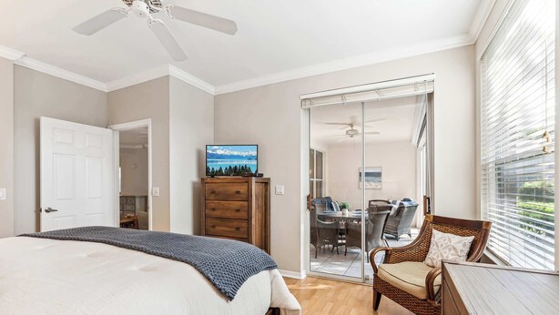 A bedroom with a bed, a dresser, a television, and a view of a dining area through a glass door. - Desired Pelican Landing First Floor Coach Home (Bonita Springs)