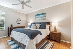 A bedroom with a bed, nightstands, a ceiling fan, a window, and a painting on the wall.