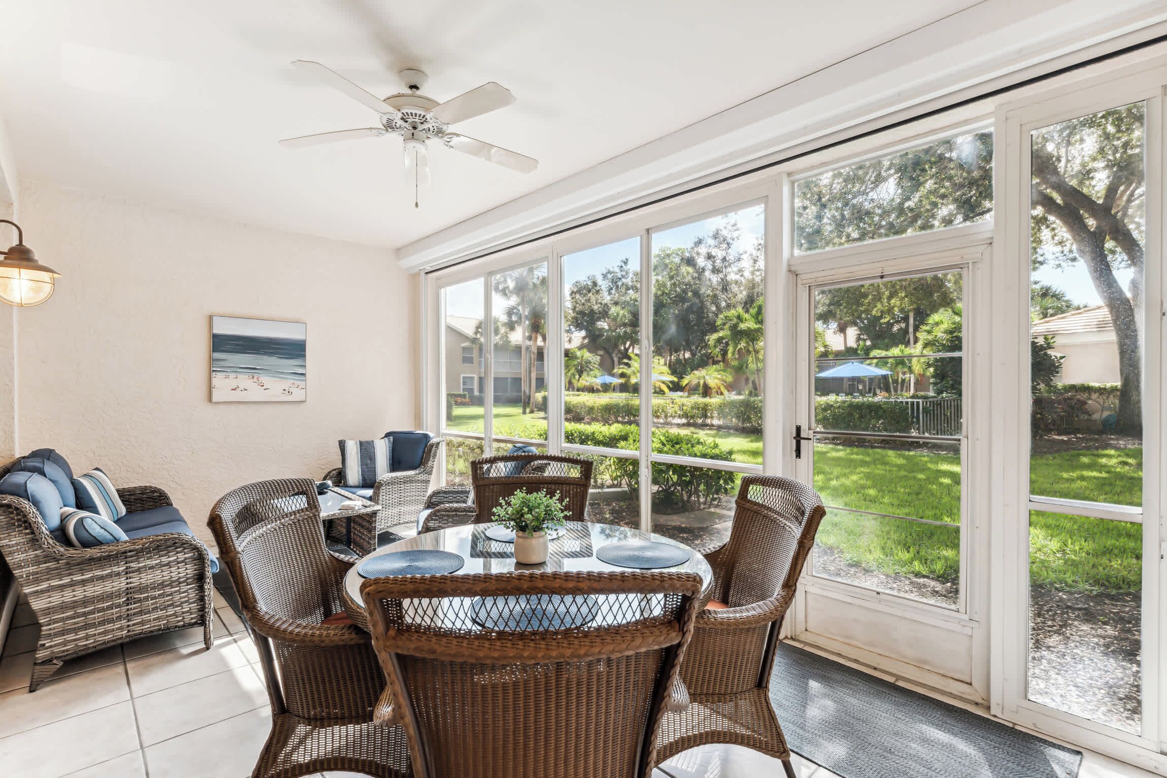 A sunlit room with a glass door leading to a garden, wicker furniture, and a ceiling fan.