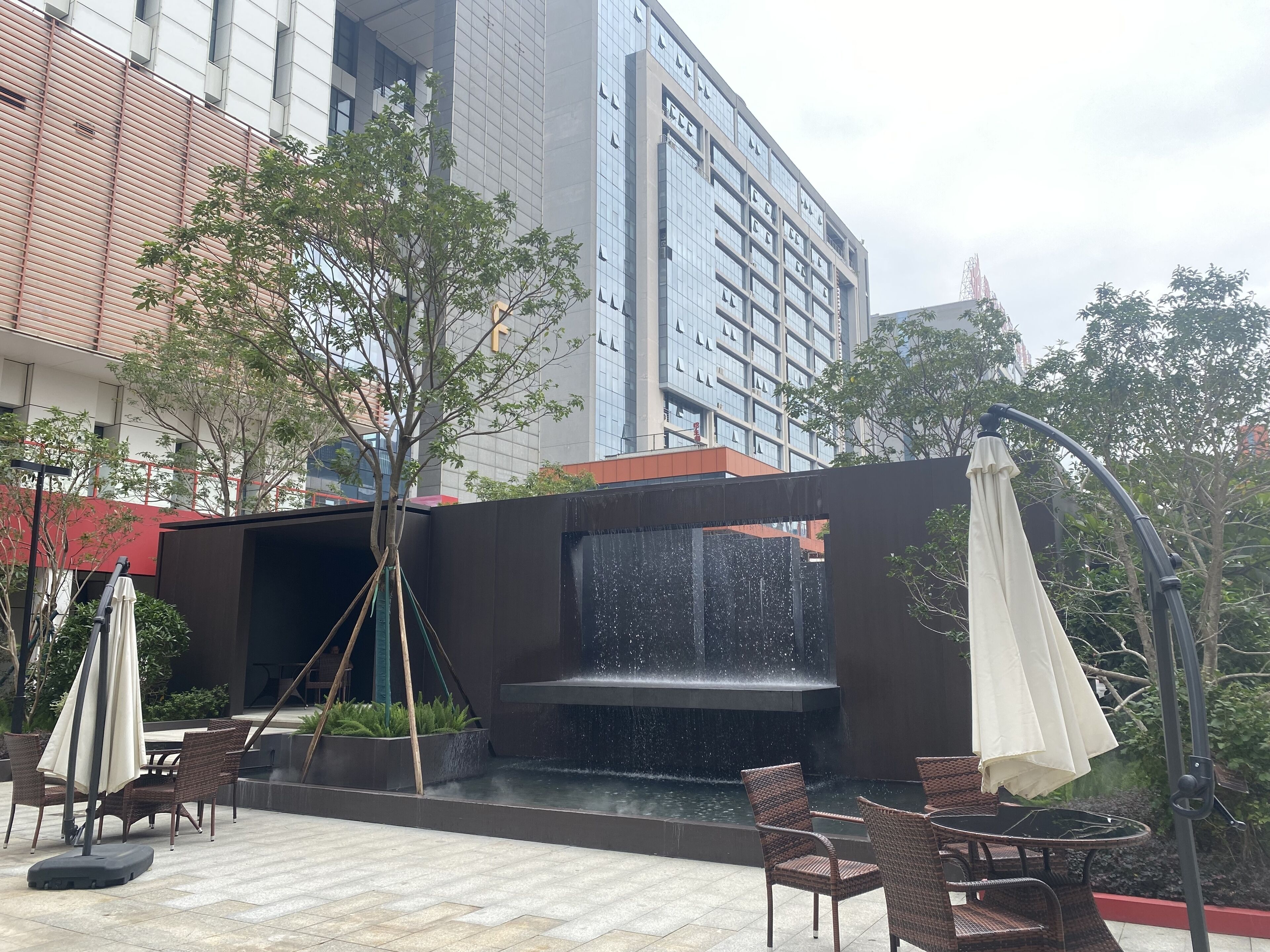 An outdoor seating area with a water feature, surrounded by trees and modern buildings.