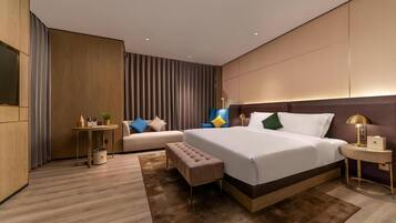 Una habitación de hotel moderna con una cama grande, una mesita de noche, un banco, una pequeña mesa con una lámpara y un sofá.