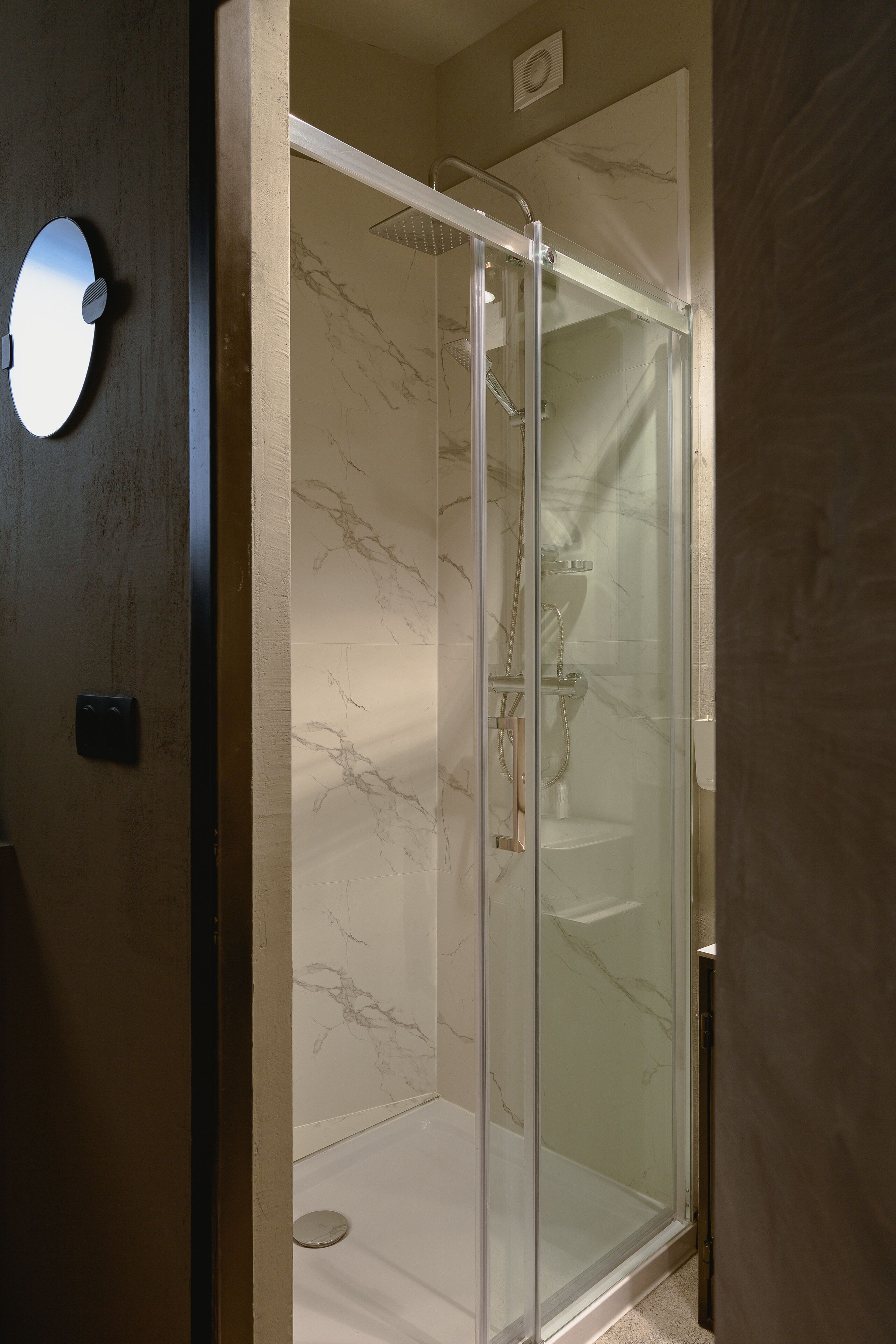 A glass-enclosed shower with a marble wall, a visible showerhead, and a control panel on the wall.