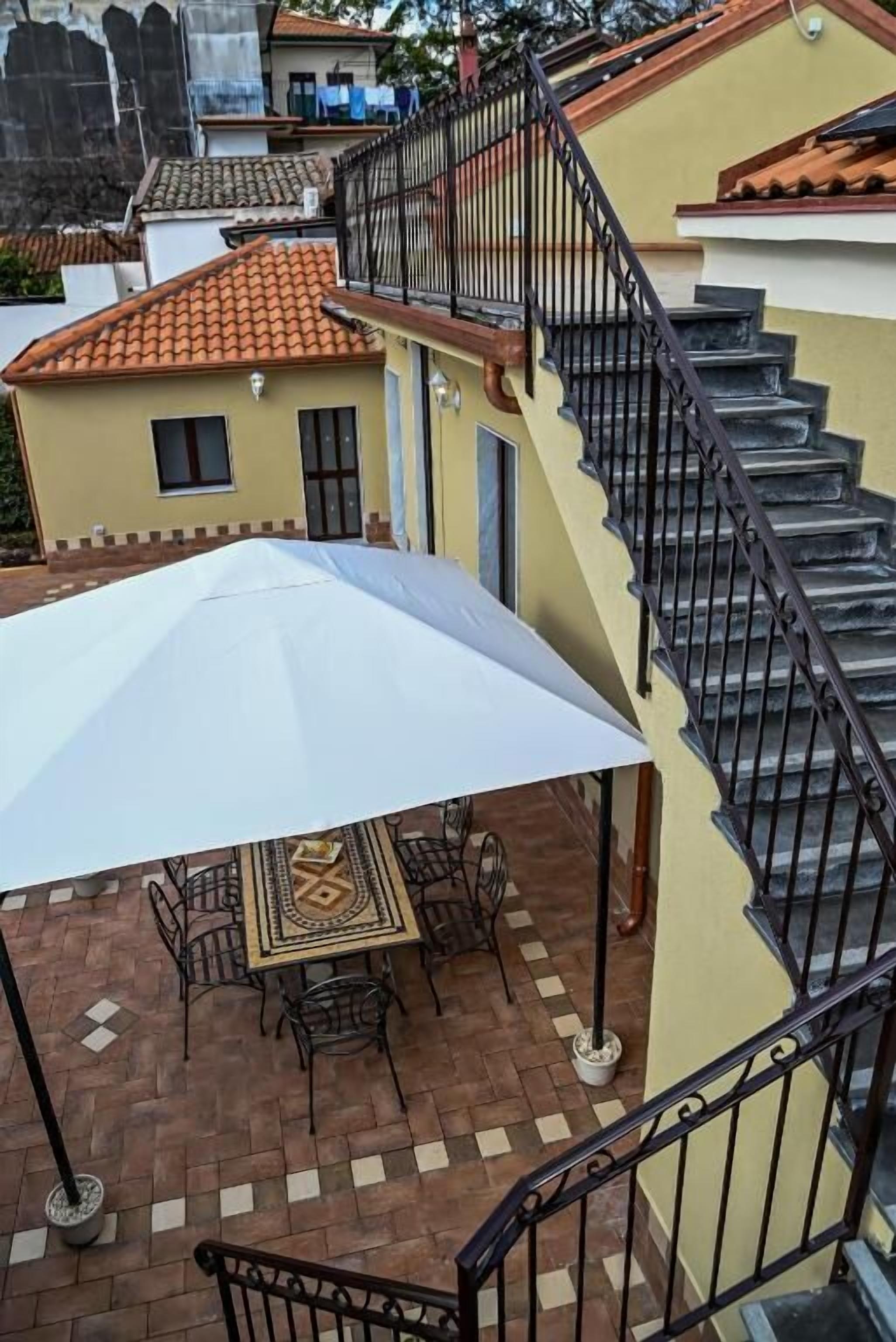 A patio area with a table and chairs, a white umbrella, and a staircase with black railings.