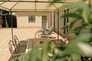 An outdoor patio with a table and chairs, a covered area, and a building in the background. - Etna Dimora dei Saponari (Trecastagni)