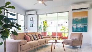 En stue med en beige sofa, et rundt sofabord og en potteplante.