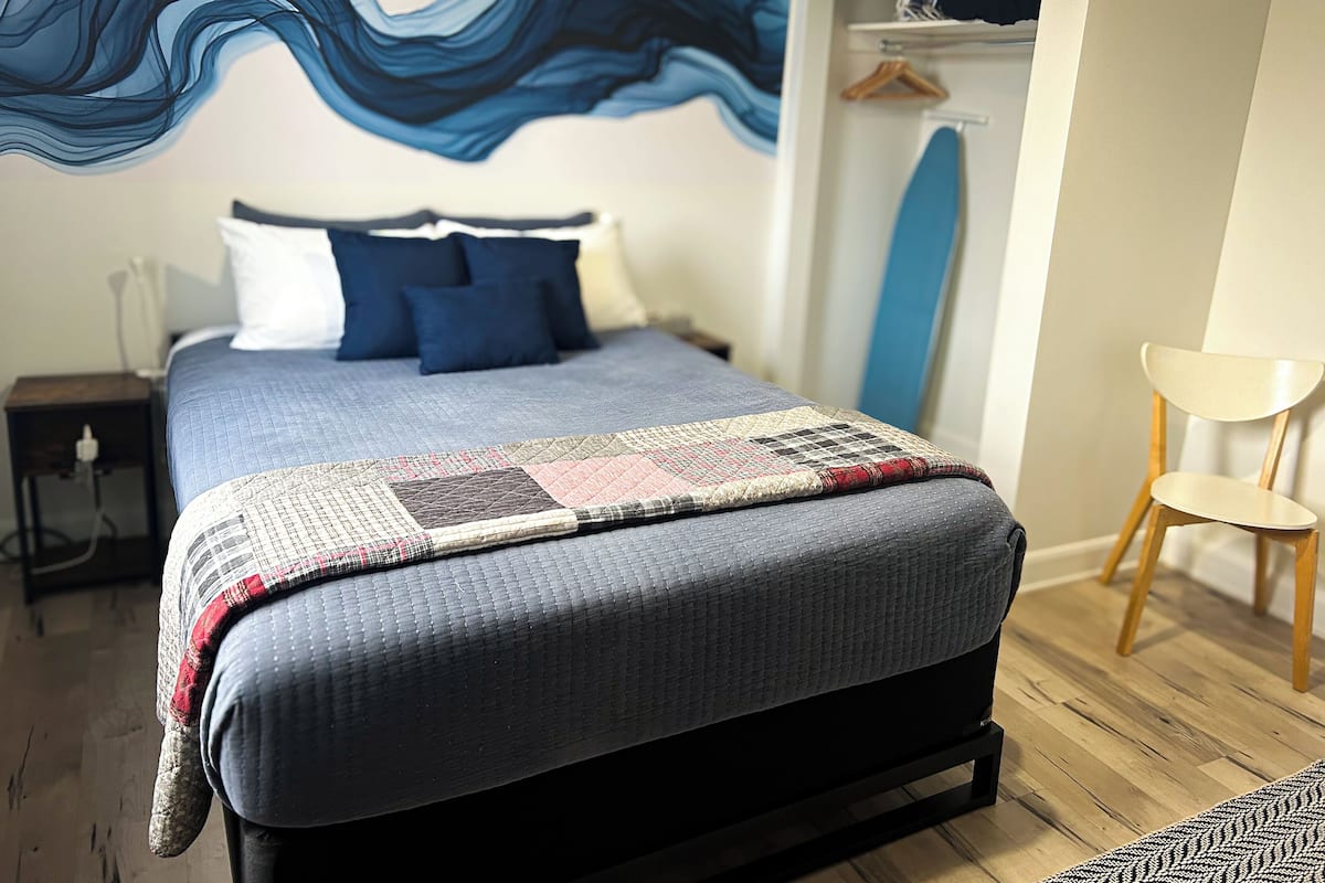 A neatly made bed with a blue quilt, a patterned throw blanket, and a blue and white pillow set.