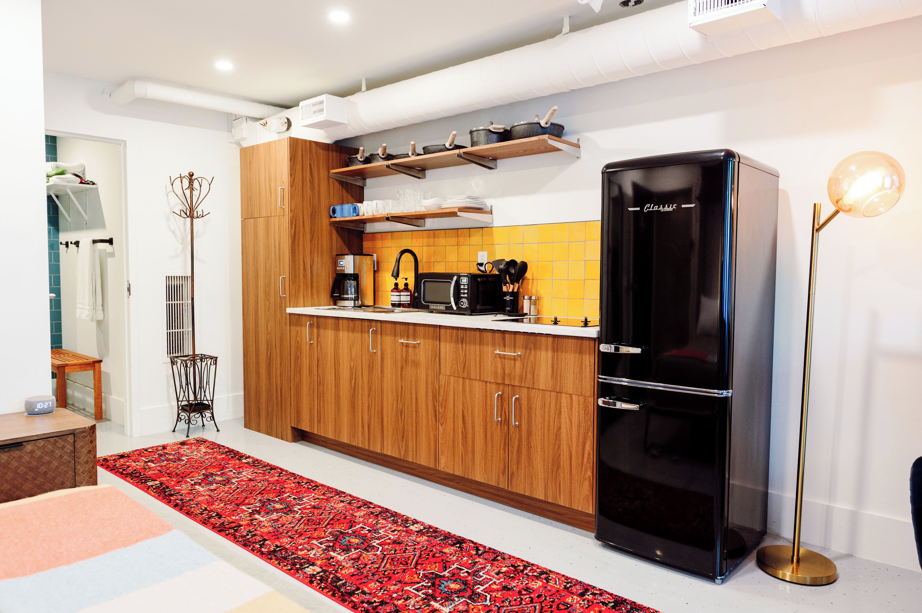 Une cuisine moderne avec des meubles en bois, un réfrigérateur noir et un tapis rouge à motifs.