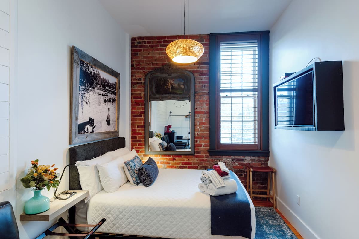 A bedroom with a bed, a mirror, a TV, and a window with blinds.