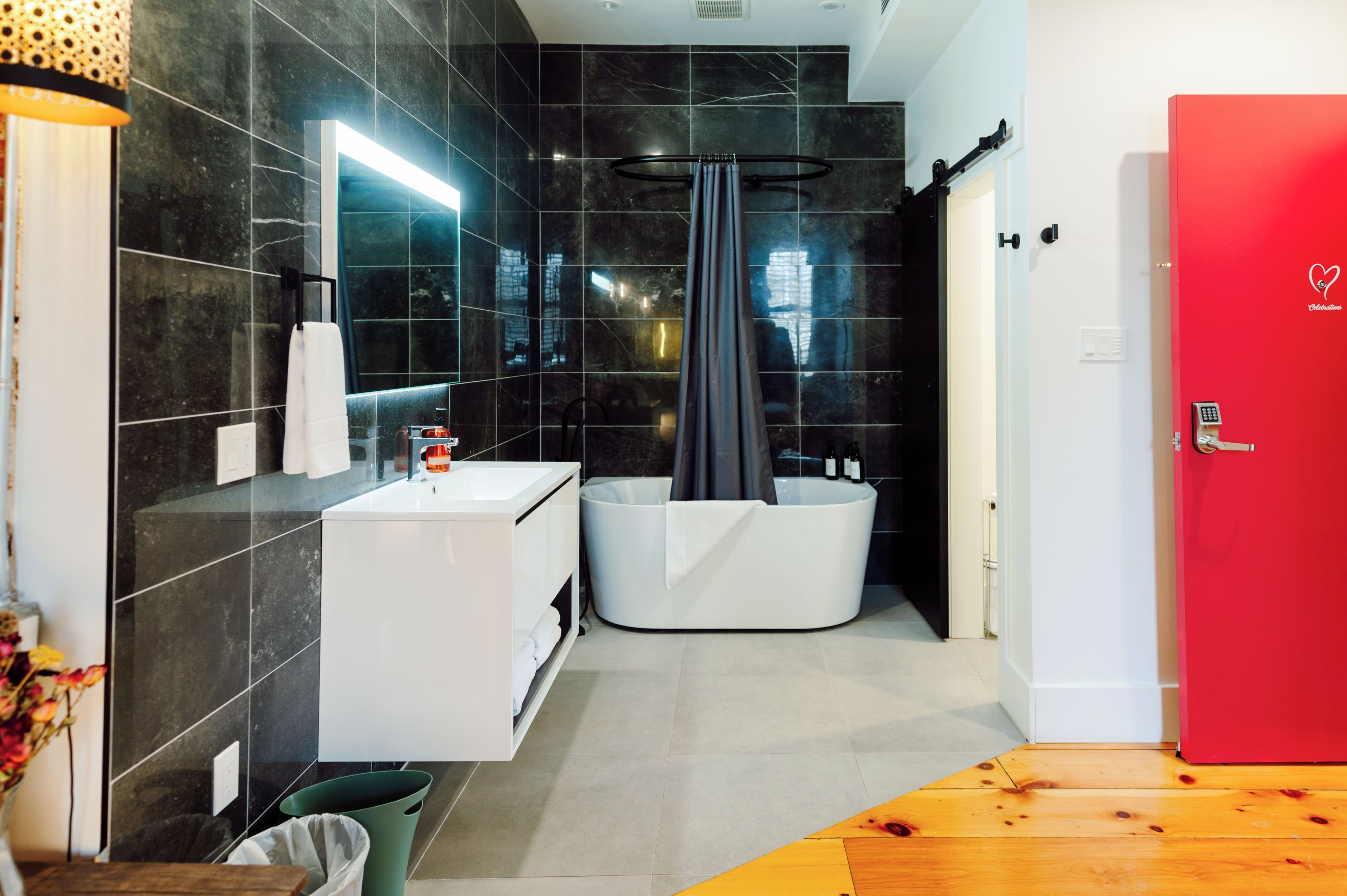 Un baño moderno con un tocador blanco, una bañera grande y una puerta roja.