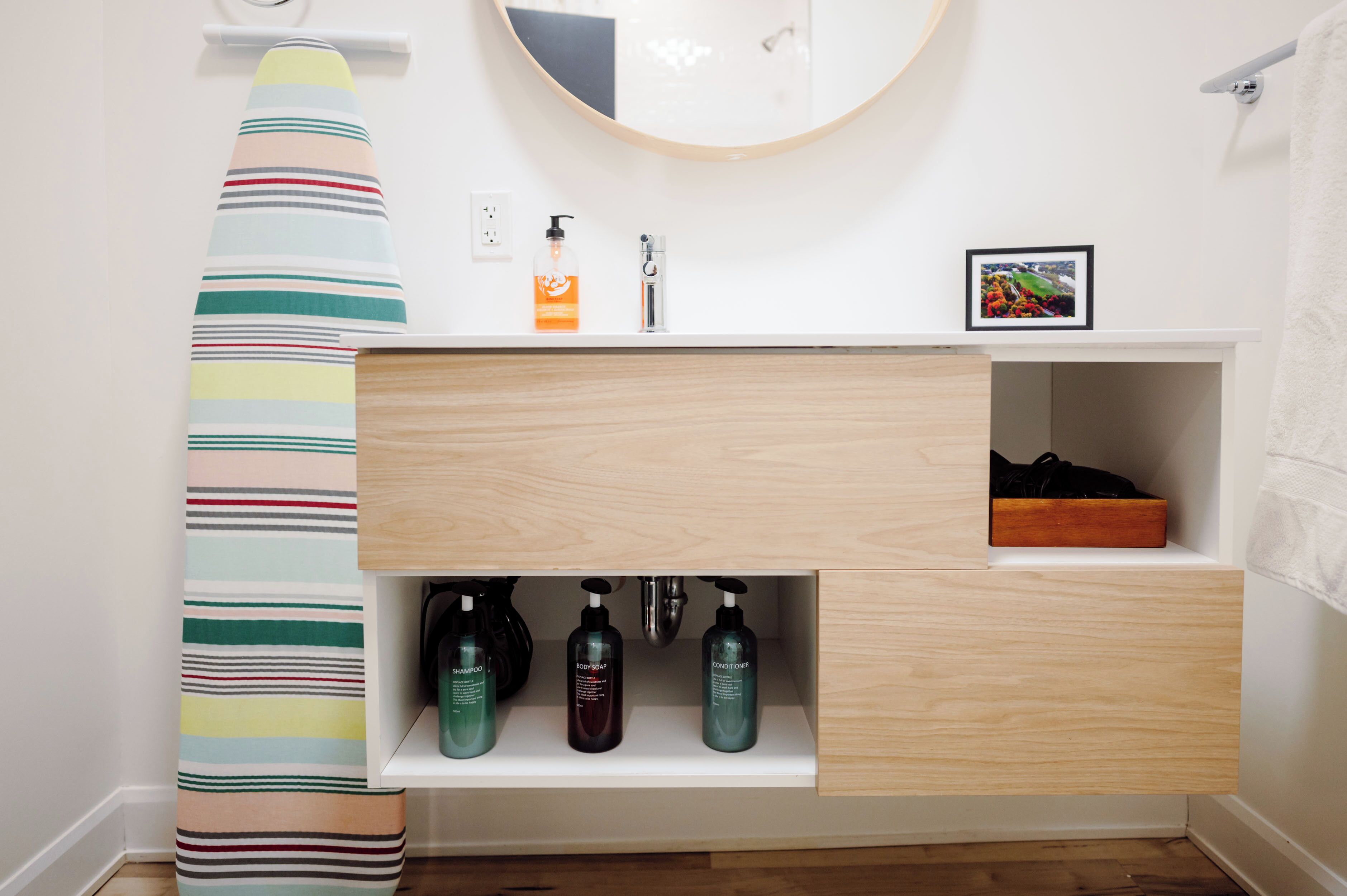 A bathroom with a striped towel, a sink with a mirror, and three bottles of shampoo, conditioner, and body wash.