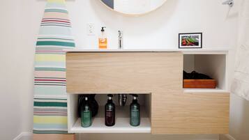 A bathroom with a striped towel, a sink with a mirror, and three bottles of shampoo, conditioner, and body wash.