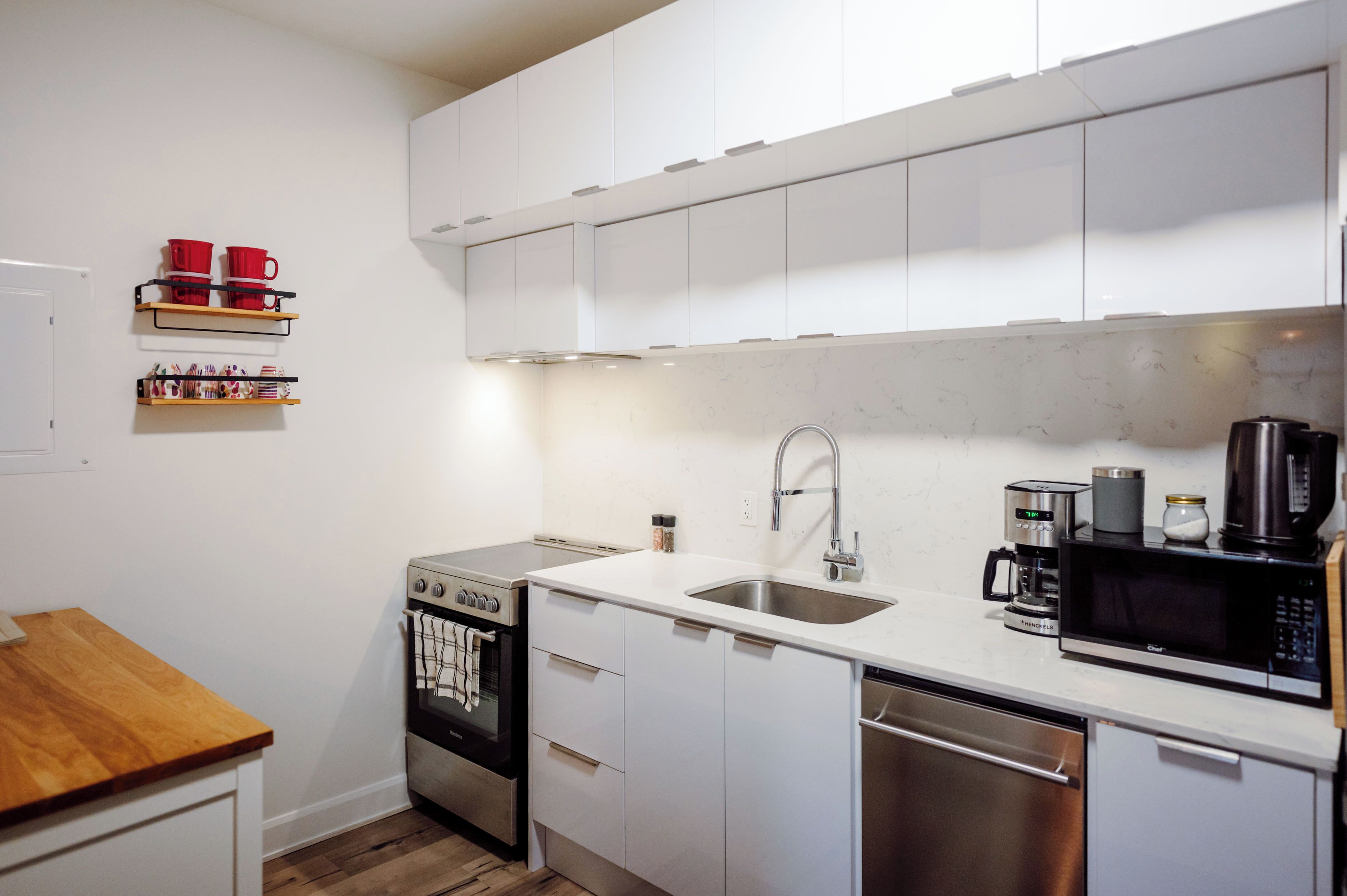 Una cocina moderna con armarios blancos, un lavamanos de acero inoxidable, un microondas y una cafetera.