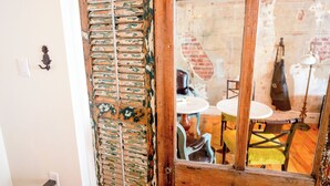 A rustic interior with a wooden door, a brick wall, and a glimpse of a dining area with a table and chairs. - Perth County Inn (Stratford)