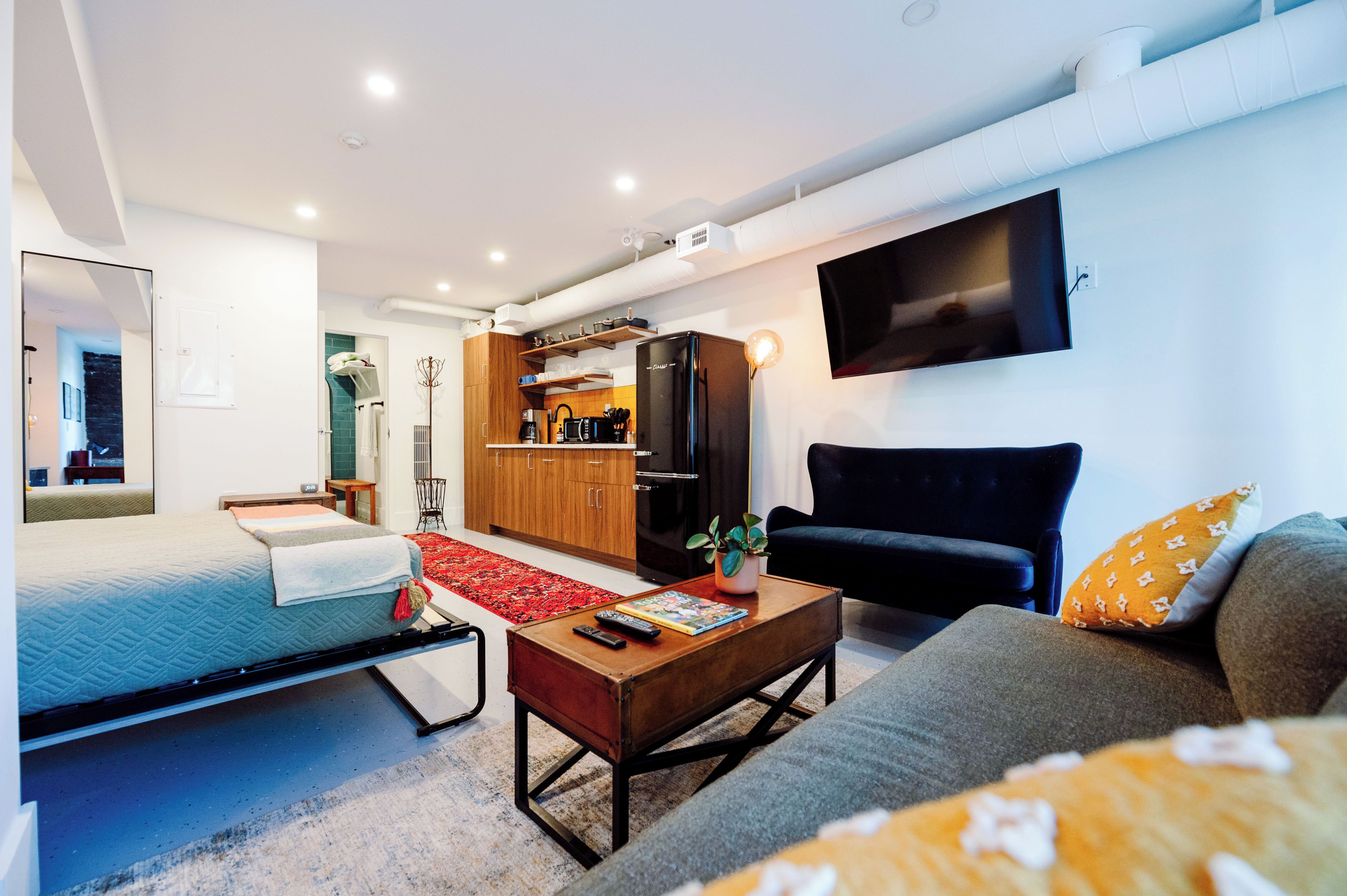A modern living room with a bed, sofa, coffee table, and a kitchen area with a refrigerator and microwave.