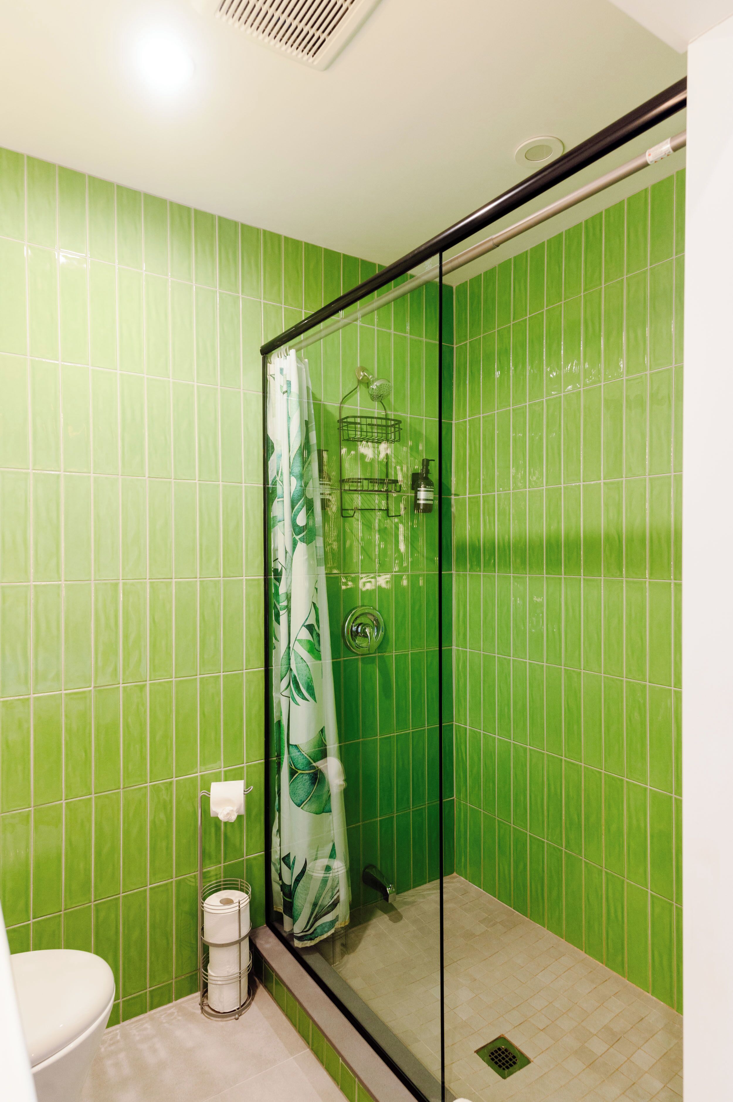 A bathroom with green tiles, a glass shower enclosure, a toilet, and a towel rack.