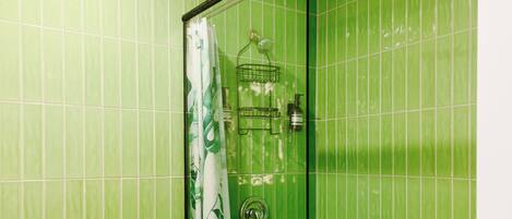 A bathroom with green tiles, a glass shower enclosure, a toilet, and a towel rack.