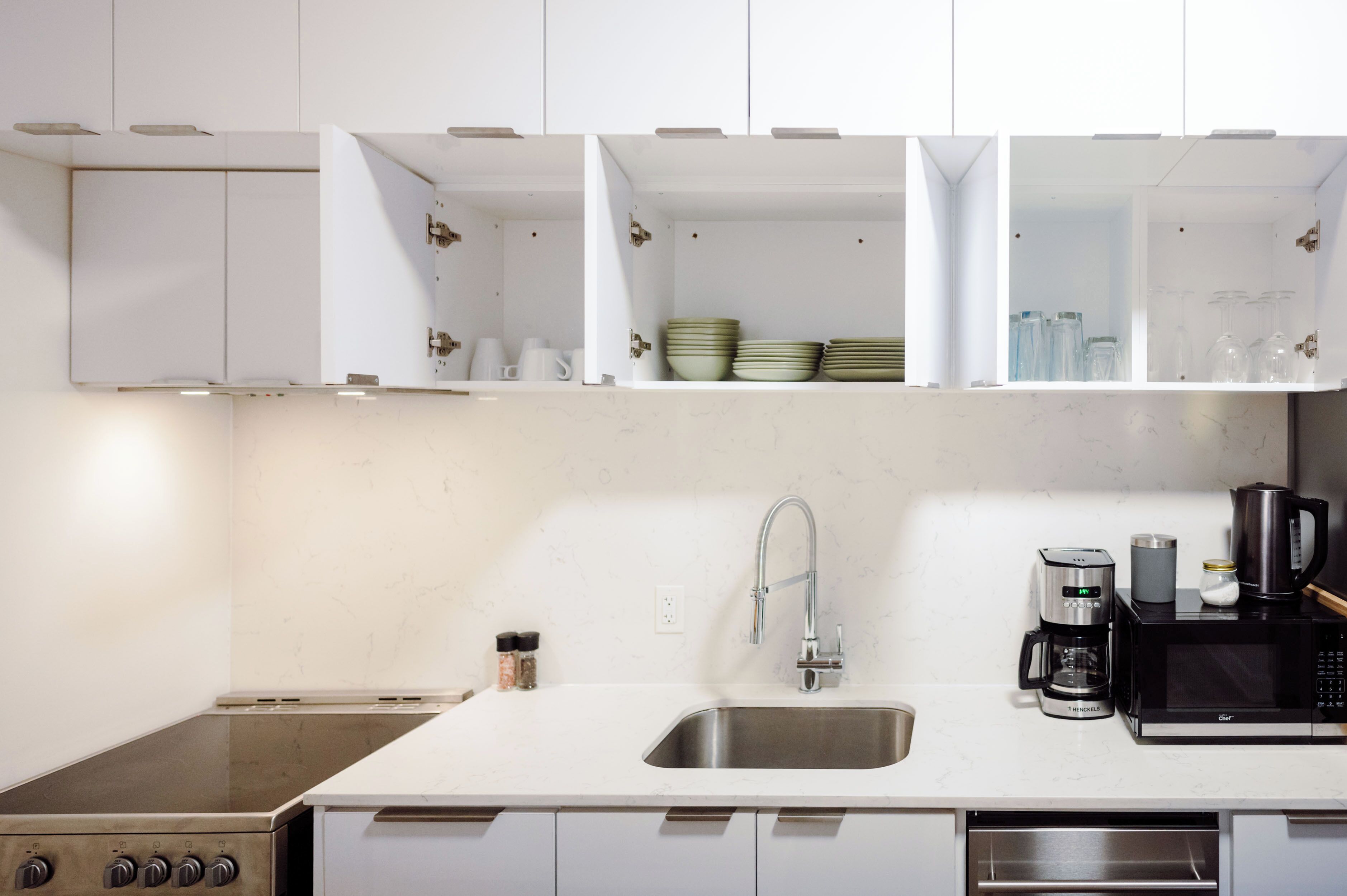 A modern kitchen with white cabinets, a stainless steel sink, a coffee maker, and a microwave.