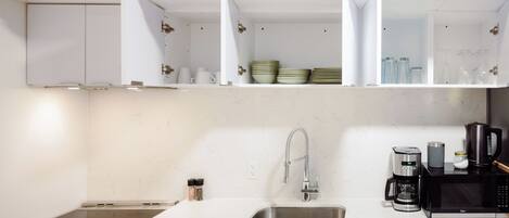 A modern kitchen with white cabinets, a stainless steel sink, a coffee maker, and a microwave.
