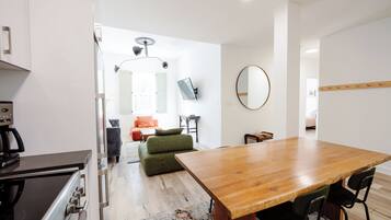 A modern kitchen with a stove, a dining table with chairs, and a sofa in the background.