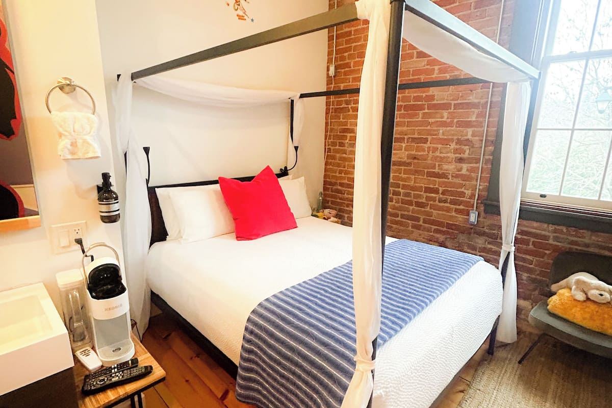 A room with a four-poster bed, a ceiling fan, a brick wall, and a window.