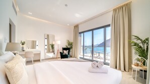 Ein modernes Hotelzimmer mit einem großen Bett, einem Schreibtisch, einem Sessel, einem Balkon mit Meerblick und einem großen Fenster.