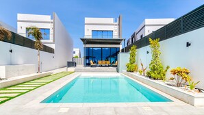 Ein moderner Poolbereich mit einem klaren blauen Pool, umgeben von weißen Wänden und einem überdachten Sitzbereich mit gelben Stühlen.