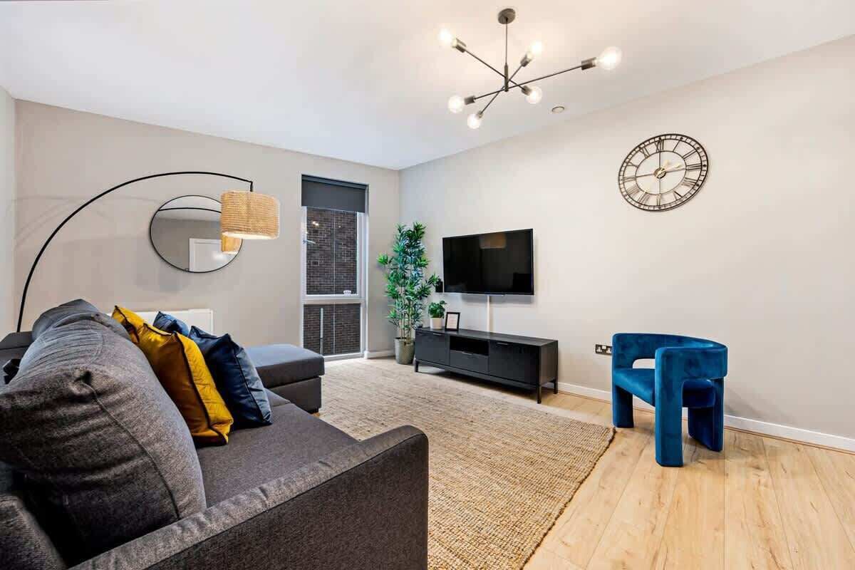A modern living room with a grey sofa, a blue chair, a black TV stand, and a large mirror.