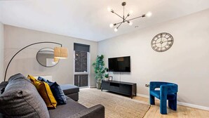 A modern living room with a grey sofa, a blue chair, a black TV stand, and a large mirror. - Host & Stay | Ropewalks Quarters II (Liverpool)