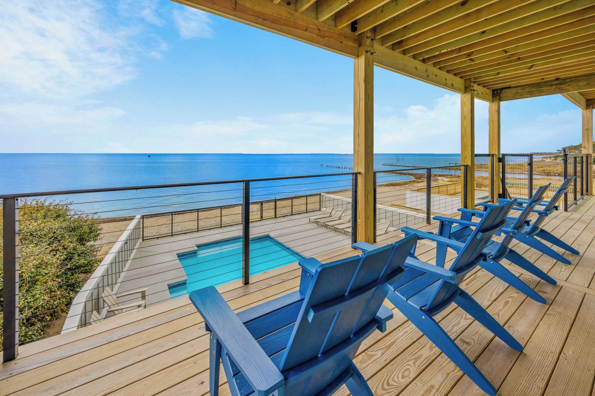 A wooden deck with a pool and lounge chairs overlooking the ocean.