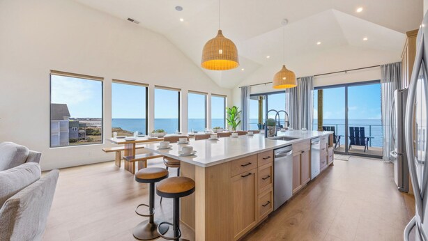 A modern kitchen with a large island, bar stools, and a view of the sea. - Premier Soundfront w/ Pool, Hot Tub, Elevator, EV Charger, Pickleball, Theater (Rodanthe)