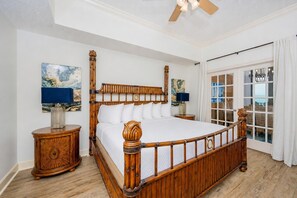 Un grand lit avec un cadre en bois, deux tables de chevet et une vue sur l’océan par une porte coulissante.