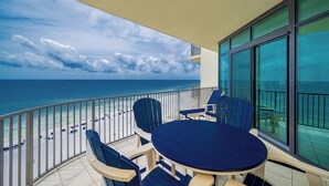 Un balcon avec une table et des chaises, donnant sur une plage animée et un ciel dégagé.