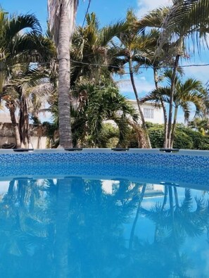 A clear blue pool surrounded by palm trees and a building in the background. - Azul príncipe  (Puerto Colombia)