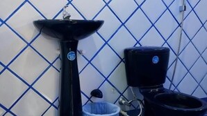 Une salle de bain avec un lavabo noir, des toilettes et une poubelle bleue.