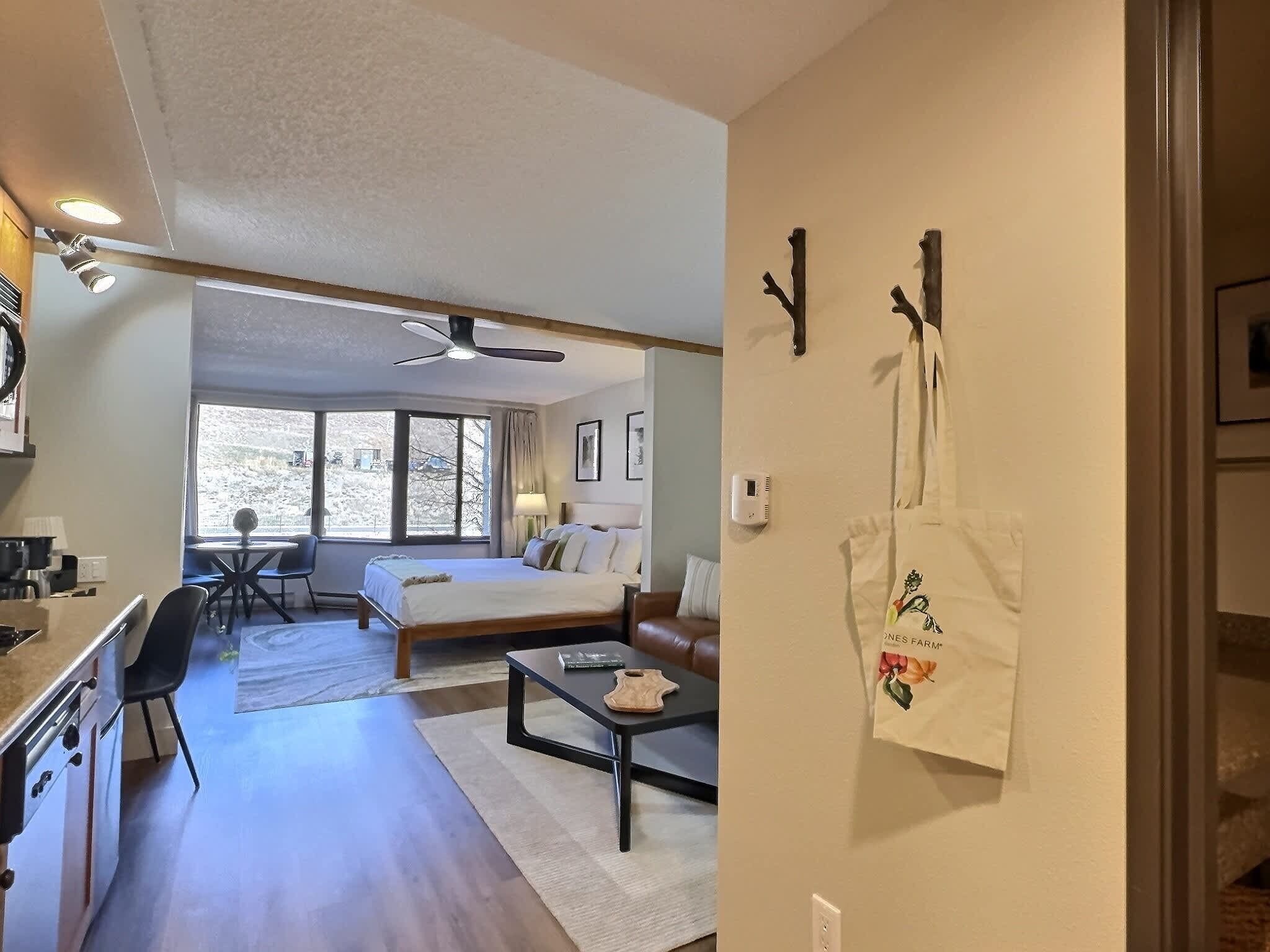 A hotel room with a bed, a desk, a chair, a coffee table, and a view of a snowy landscape through the window.