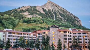 A multi-story hotel with a stone tower, surrounded by trees and a mountain backdrop.
