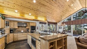 A spacious kitchen with wooden cabinets, a large island, and a dining area with a view of the outdoors. - Getting Away Together 6 Bedroom Home by RedAwning (South Lake Tahoe)