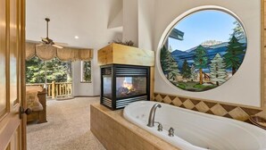 A bathroom with a large bathtub, a fireplace, and a view of trees through a stained glass window. - Getting Away Together 6 Bedroom Home by RedAwning (South Lake Tahoe)