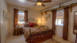 A bedroom with a bed, a ceiling fan, a bedside table with a lamp, and a window with curtains. - Breezy Pines Cabin 4 Bedroom Home by RedAwning (South Lake Tahoe)