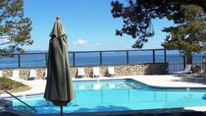 A pool with a stone wall and lounge chairs, overlooking a body of water.