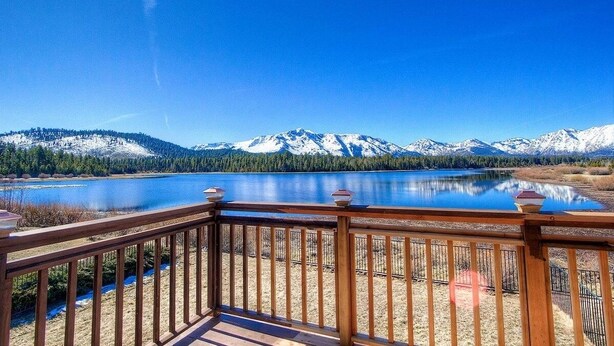 A wooden deck overlooking a lake with snow-capped mountains in the background.