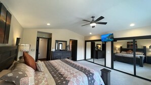 A bedroom with a large bed, a ceiling fan, a TV, and a mirror.