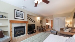 Un salon chaleureux avec une cheminée, un canapé, un coin repas et une chambre à coucher avec un lit.