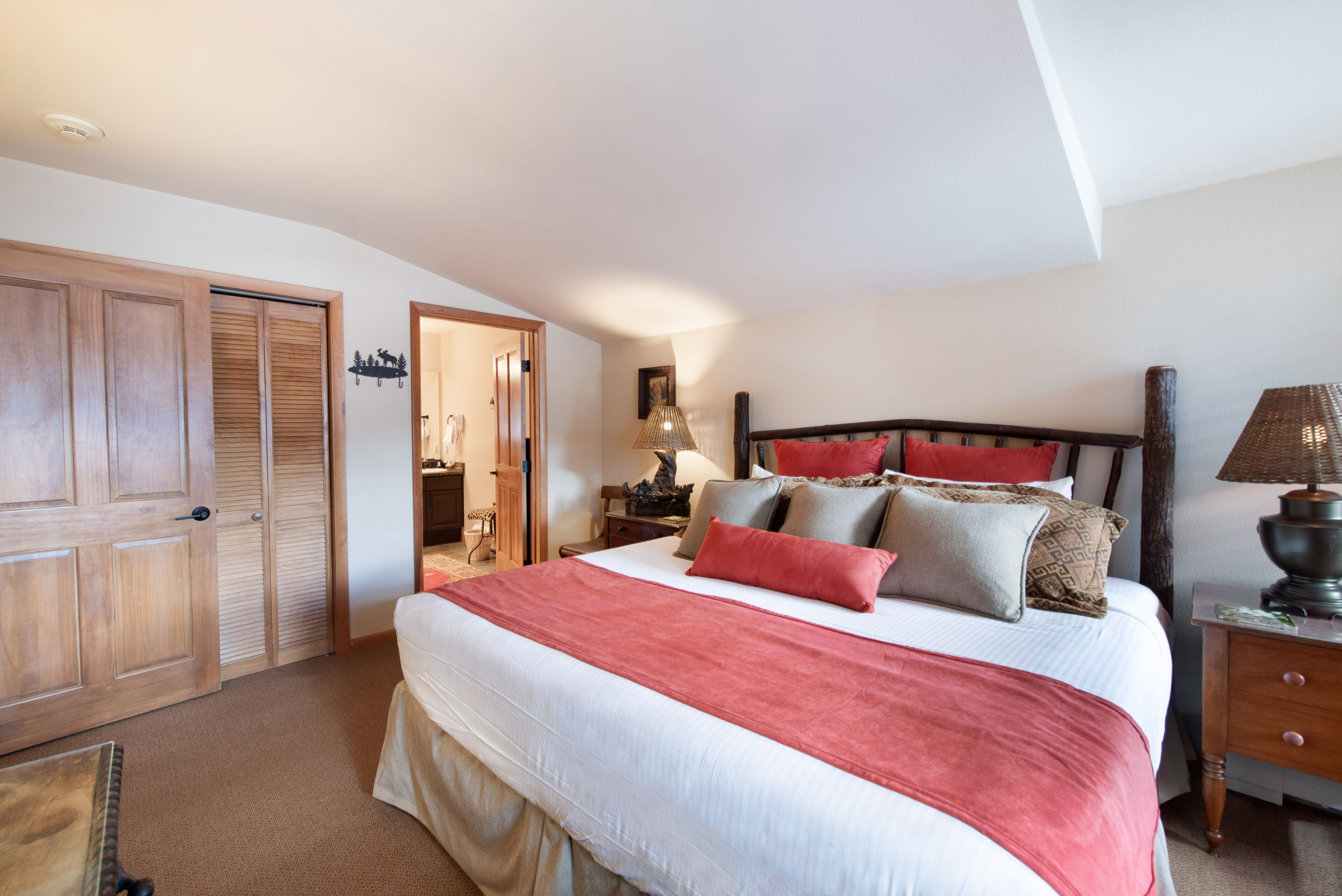A bedroom with a large bed, wooden wardrobe, and a nightstand with a lamp.