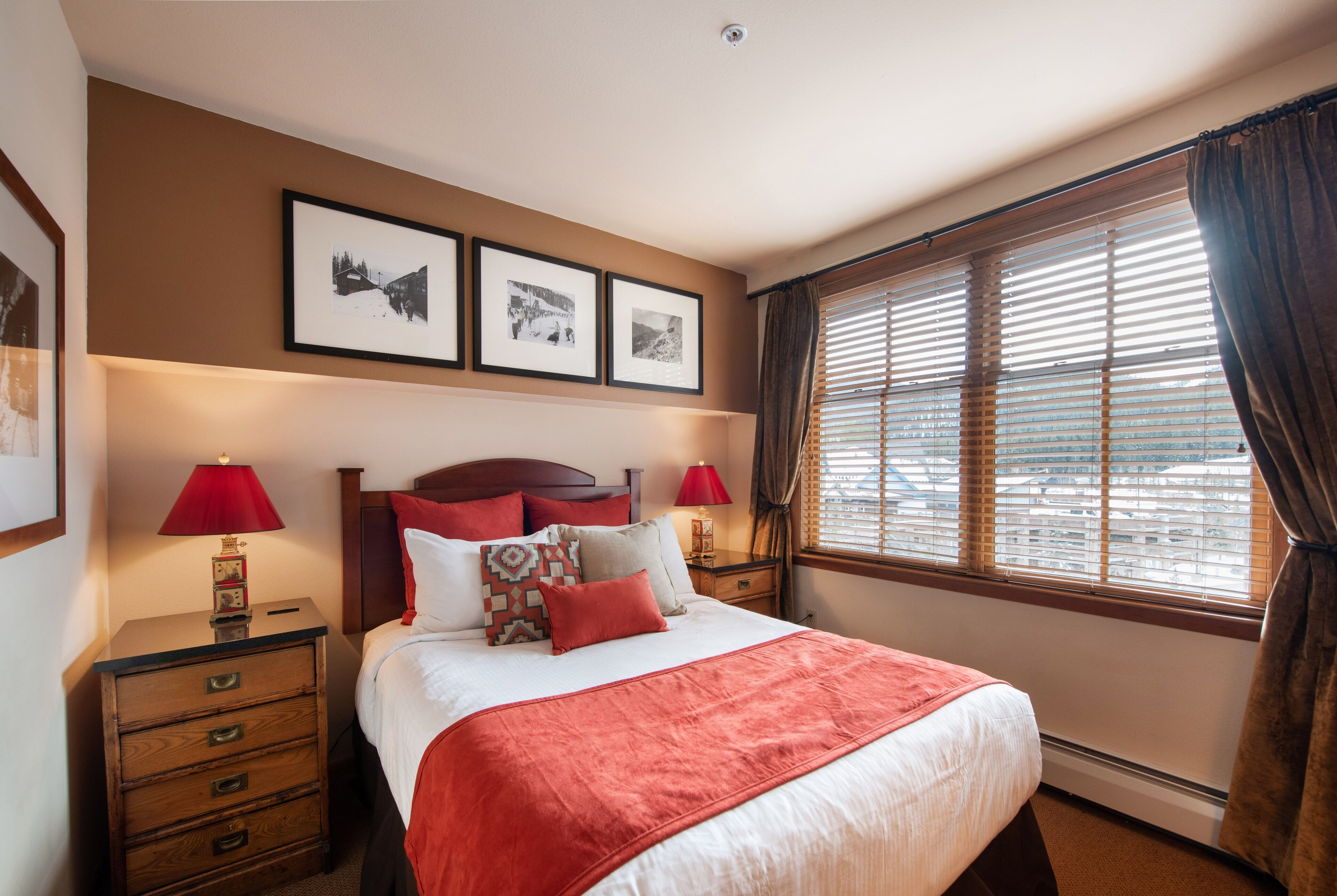 A neatly arranged bedroom with a large bed, two bedside tables, a nightstand, and a window with blinds.
